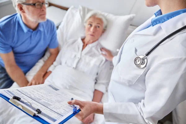 Old couple and doctor with clipboard at hospital — Stock Photo, Image