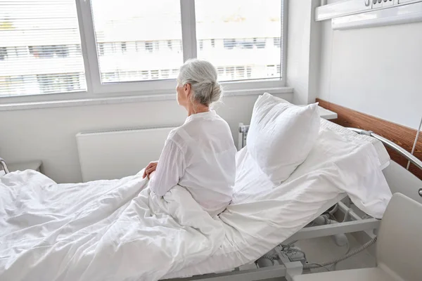 Anciana solitaria sentada en la cama en el hospital —  Fotos de Stock