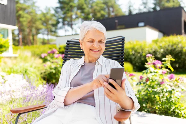 Ευτυχισμένη ηλικιωμένη γυναίκα με τηλέφωνο στον καλοκαιρινό κήπο — Φωτογραφία Αρχείου