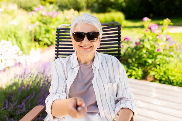 Счастливая пожилая женщина делает селфи в летнем саду — стоковое фото