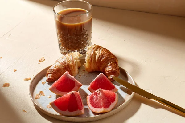 Bicchiere di caffè, croissant e pompelmo sul tavolo — Foto Stock