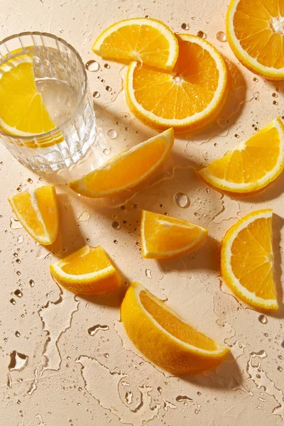 Vaso de agua y rodajas de naranja sobre mesa húmeda — Foto de Stock