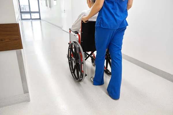 Медсестра со старшим пациентом в инвалидной коляске в клинике — стоковое фото