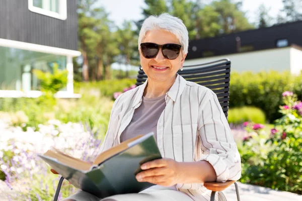 Счастливая пожилая женщина читает книгу в летнем саду — стоковое фото