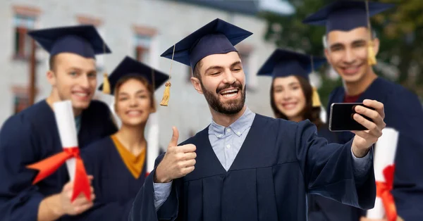 Estudiantes graduados con smartphone tomando selfie —  Fotos de Stock