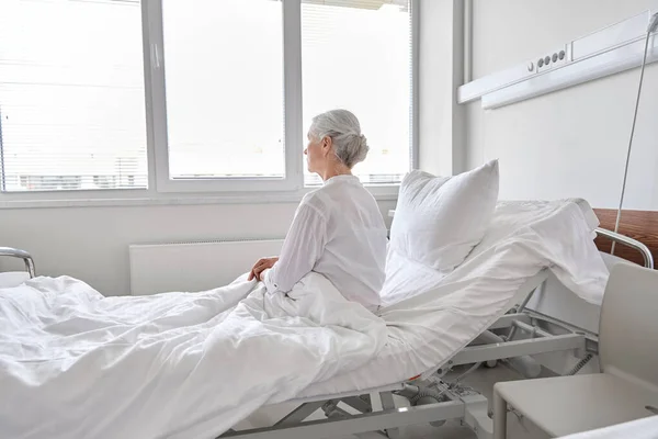 Anciana solitaria sentada en la cama en el hospital —  Fotos de Stock
