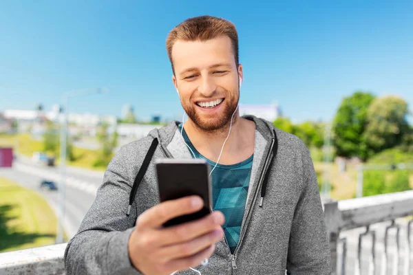 Kulaklıklı ve akıllı telefonlu gülümseyen genç adam. — Stok fotoğraf