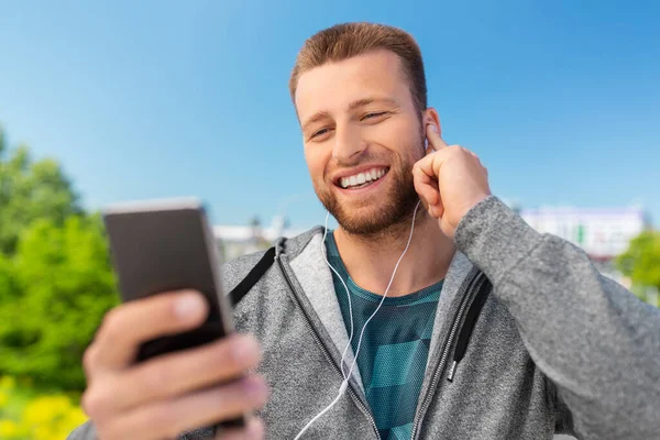 Jeune homme souriant avec écouteurs et smartphone — Photo