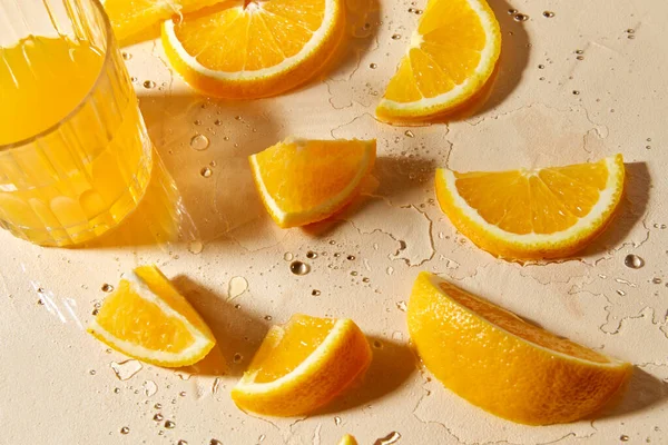 Glass of juice and orange slices on wet table — Stock Photo, Image