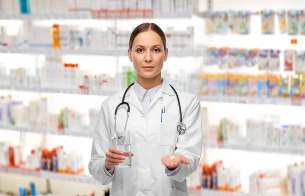 Médico con pastillas y vaso de agua en la farmacia —  Fotos de Stock