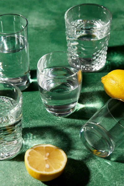 Glazen met water en citroenen op groene achtergrond — Stockfoto