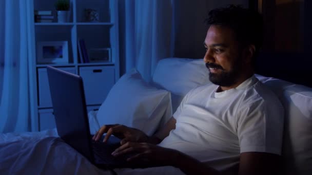 Чоловік з ноутбуком у ліжку вночі. — стокове відео