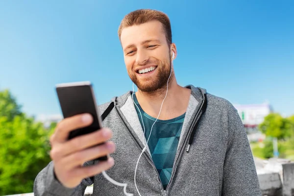 Usmívající se mladý muž se sluchátky a smartphonem — Stock fotografie