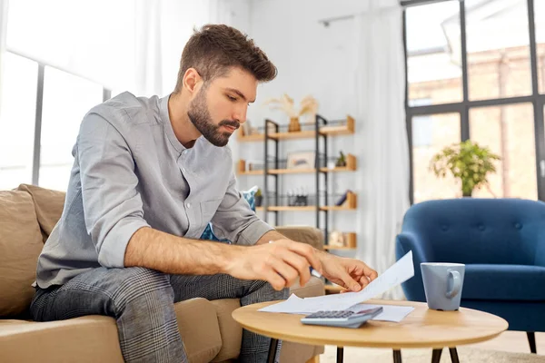 Man with bills counting on calculator at home — Stock Photo, Image