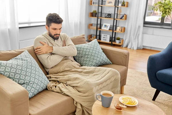 Malade jeune homme en couverture boire du thé chaud à la maison — Photo