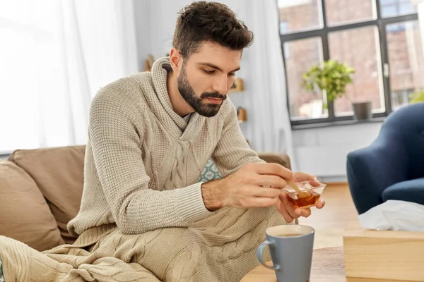 Zieke jongeman in deken drinken hete thee thuis — Stockfoto