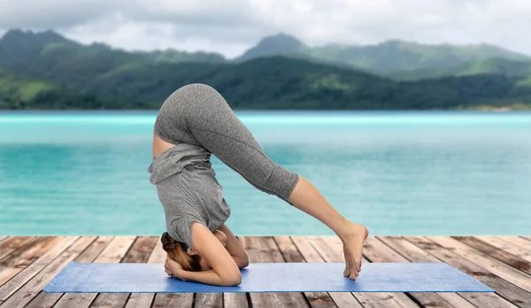 Kadın amuda kalkmış yoga yapıyor. Okyanusun üstünde poz veriyor. — Stok fotoğraf