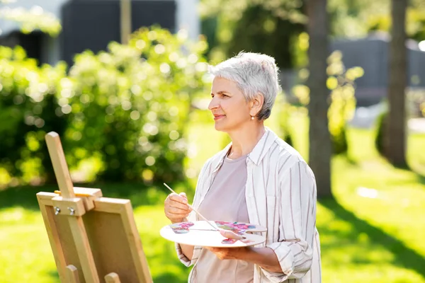 Starsza kobieta z sztalugami malowanie na zewnątrz — Zdjęcie stockowe