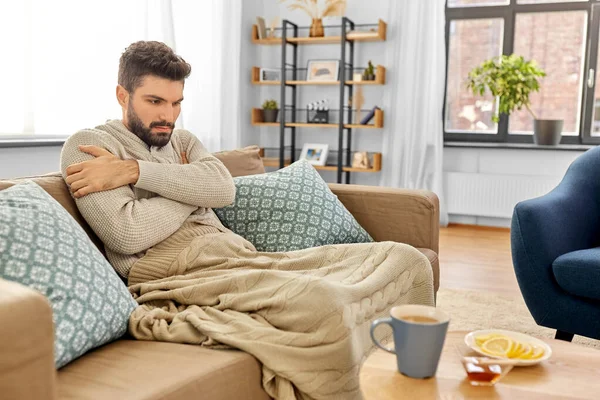 Zieke jongeman in deken drinken hete thee thuis — Stockfoto