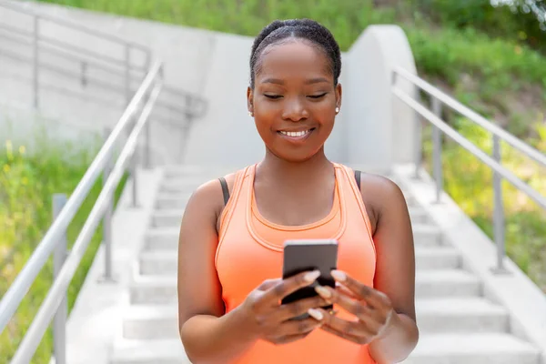 Glimlachende sportieve Afrikaanse vrouw met behulp van smartphone — Stockfoto