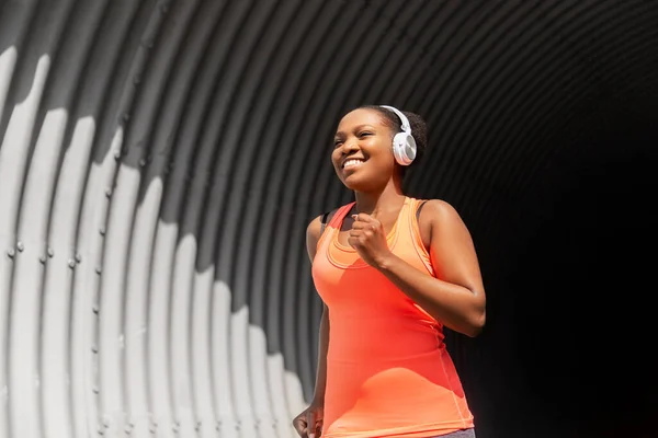 Femme africaine heureuse dans les écouteurs courir à l'extérieur — Photo