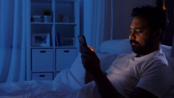 Hombre indio con teléfono inteligente en la cama en casa por la noche — Vídeo de stock