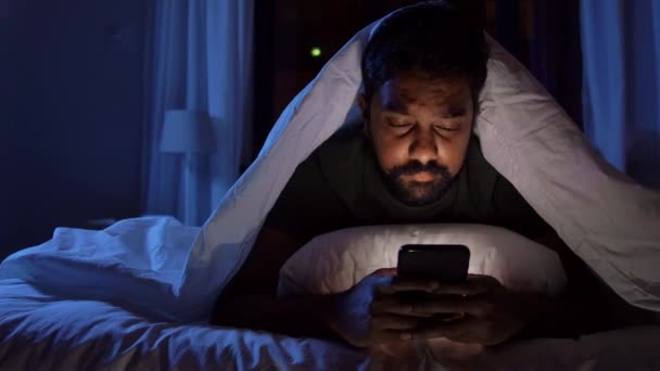 Indian man with smartphone in bed at home at night — Stock Video