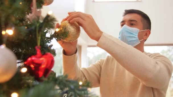 Homem em máscara decorando árvore de natal em casa — Vídeo de Stock