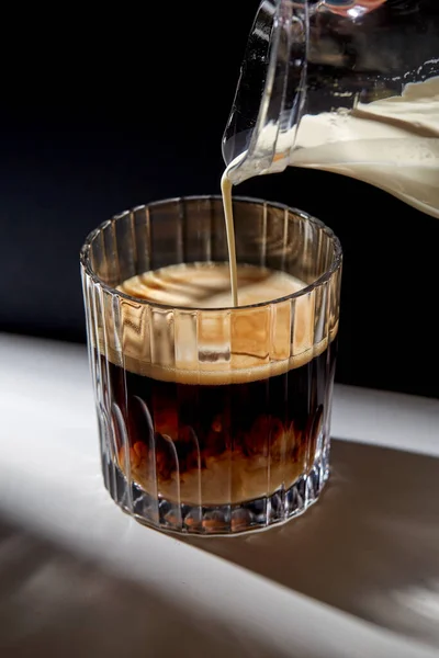 Hand met kruik gieten crème om glas koffie — Stockfoto
