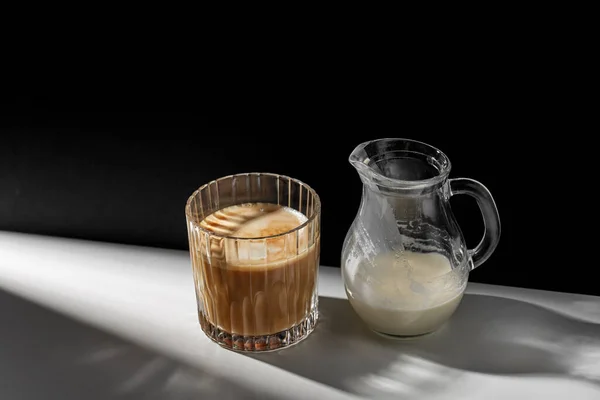 Koffie in glas en kan melk of room op tafel — Stockfoto