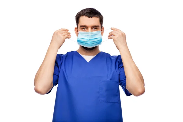 Doctor masculino en uniforme azul poniéndose la máscara — Foto de Stock