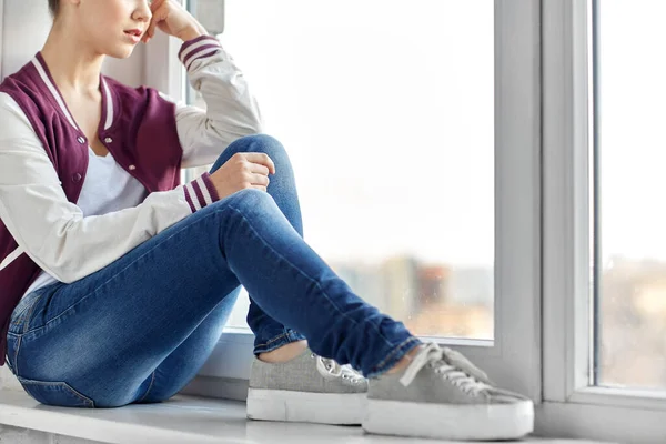 Sad teenage girl sitting on window sill — Stock Photo, Image