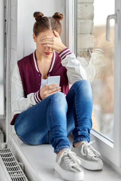 Tonårstjej med smartphone sittande på fönsterbrädan — Stockfoto