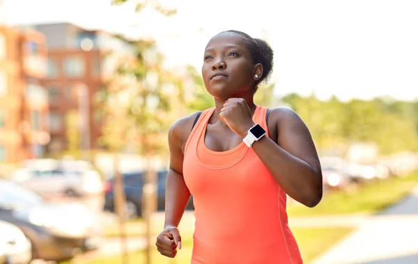 Mujer africana con reloj inteligente corriendo en la ciudad — Foto de Stock