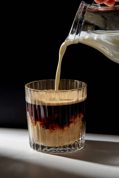 Hand with jug pouring cream to glass of coffee — Stock Photo, Image