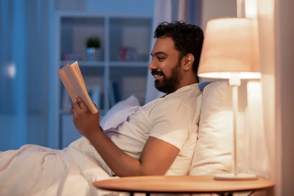 Hombre indio feliz leyendo libro en la cama por la noche — Foto de Stock