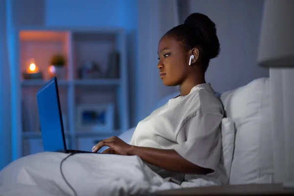 Frau mit Laptop und Kopfhörer nachts im Bett — Stockfoto