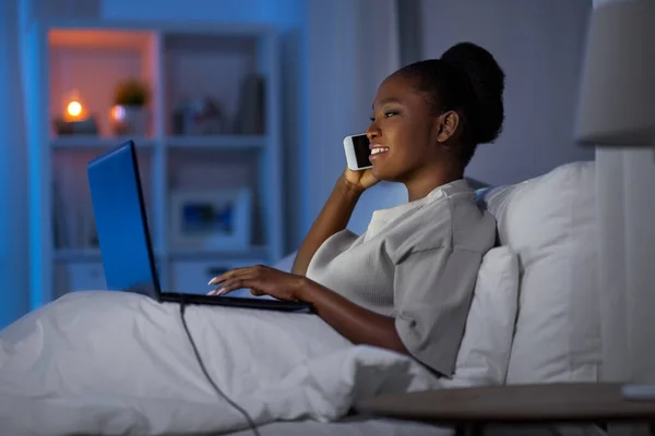 Nő laptop hívás okostelefon az ágyban — Stock Fotó