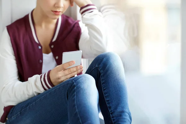 Tonårstjej med smartphone sittande på fönsterbrädan — Stockfoto