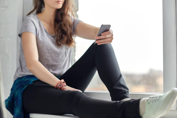 Adolescente com smartphone sentado no peitoril da janela — Fotografia de Stock