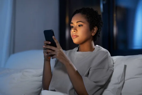 Afrikanerin mit Smartphone nachts im Bett — Stockfoto