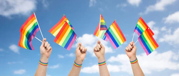 Mãos com orgulho gay bandeiras do arco-íris e pulseira — Fotografia de Stock