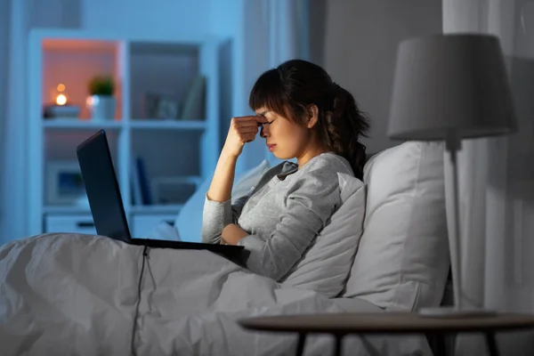 Mulher estressada com laptop trabalhando na cama à noite — Fotografia de Stock