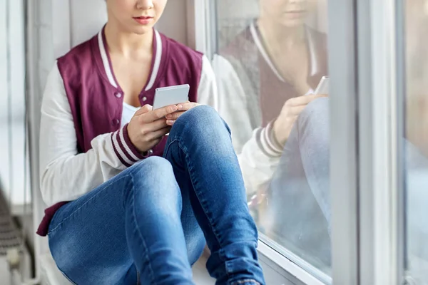Девочка-подросток со смартфоном сидит на подоконнике — стоковое фото