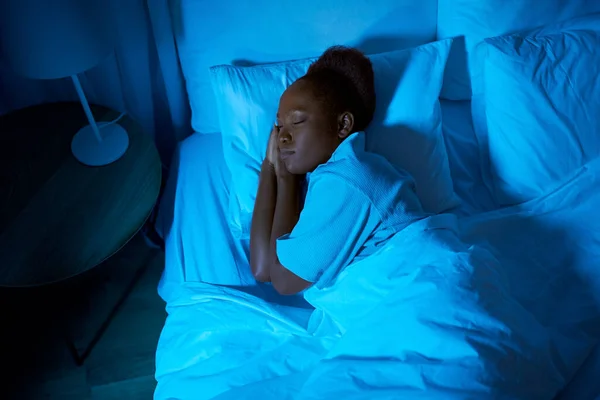 Mujer africana durmiendo en la cama en casa por la noche —  Fotos de Stock