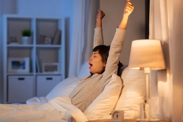 Cansado asiático mujer estiramiento en cama en la noche —  Fotos de Stock