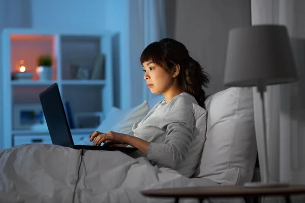 Mulher com laptop na cama em casa à noite — Fotografia de Stock