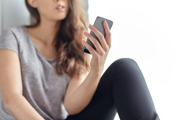 Adolescente com smartphone sentado na janela — Fotografia de Stock