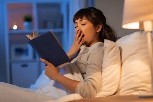 피곤 한 동양 여자가 집 침대에서 책을 읽고 있었다 — 스톡 사진