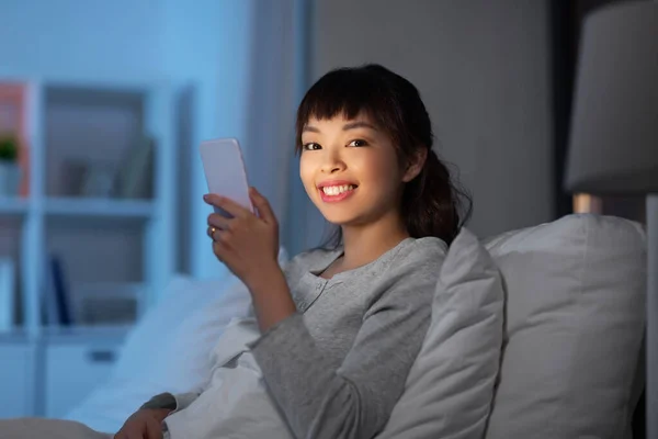 Aziatische vrouw met smartphone in bed 's nachts — Stockfoto